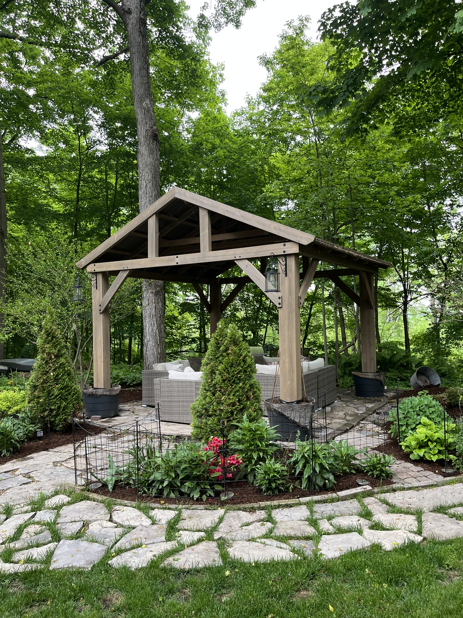 Timber pavilion with lounge seating on a flagstone patio in a wooded backyard garden