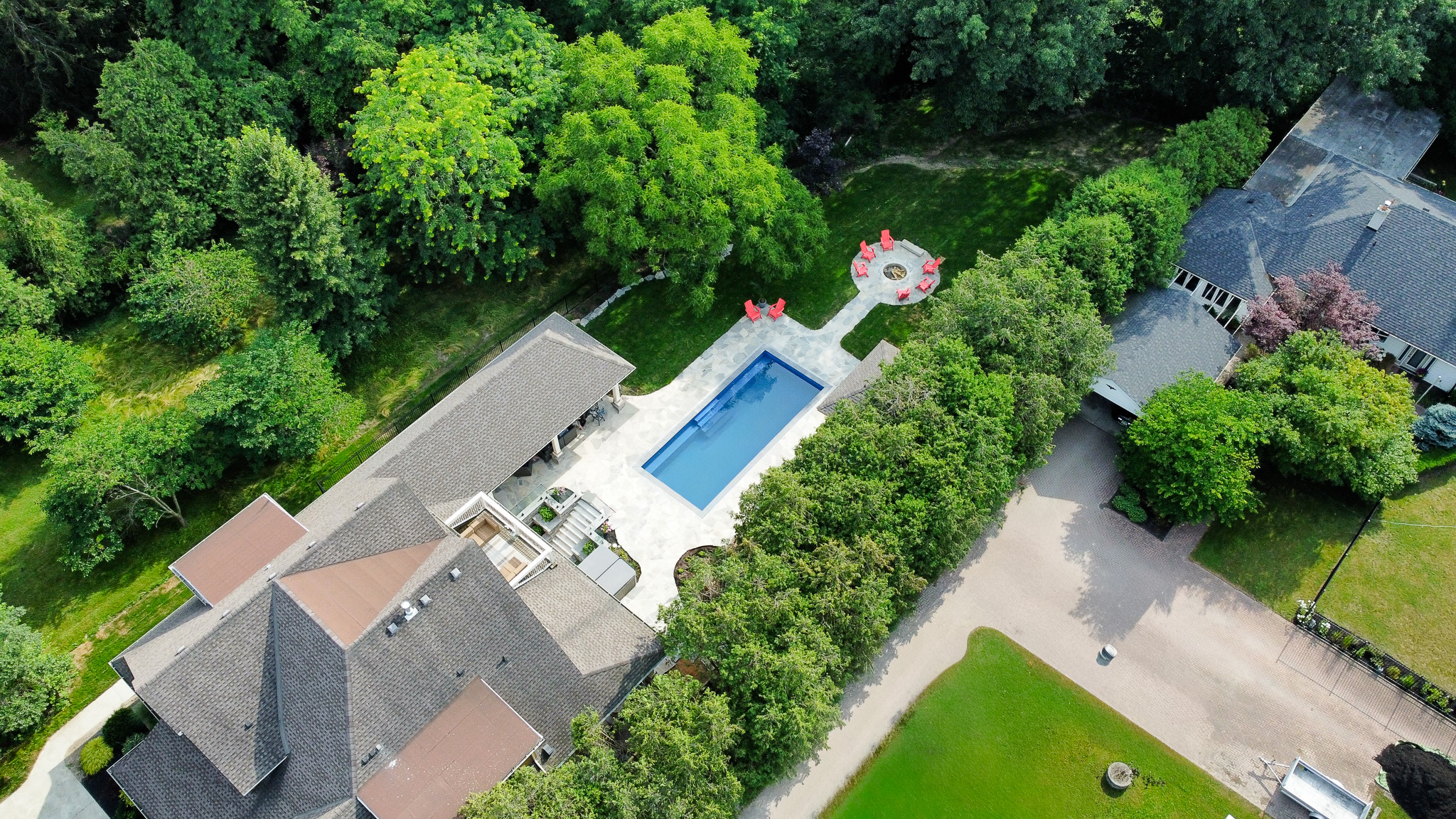 Aerial view of a backyard pool and flagstone patio with a fire-pit lounge, framed by mature trees