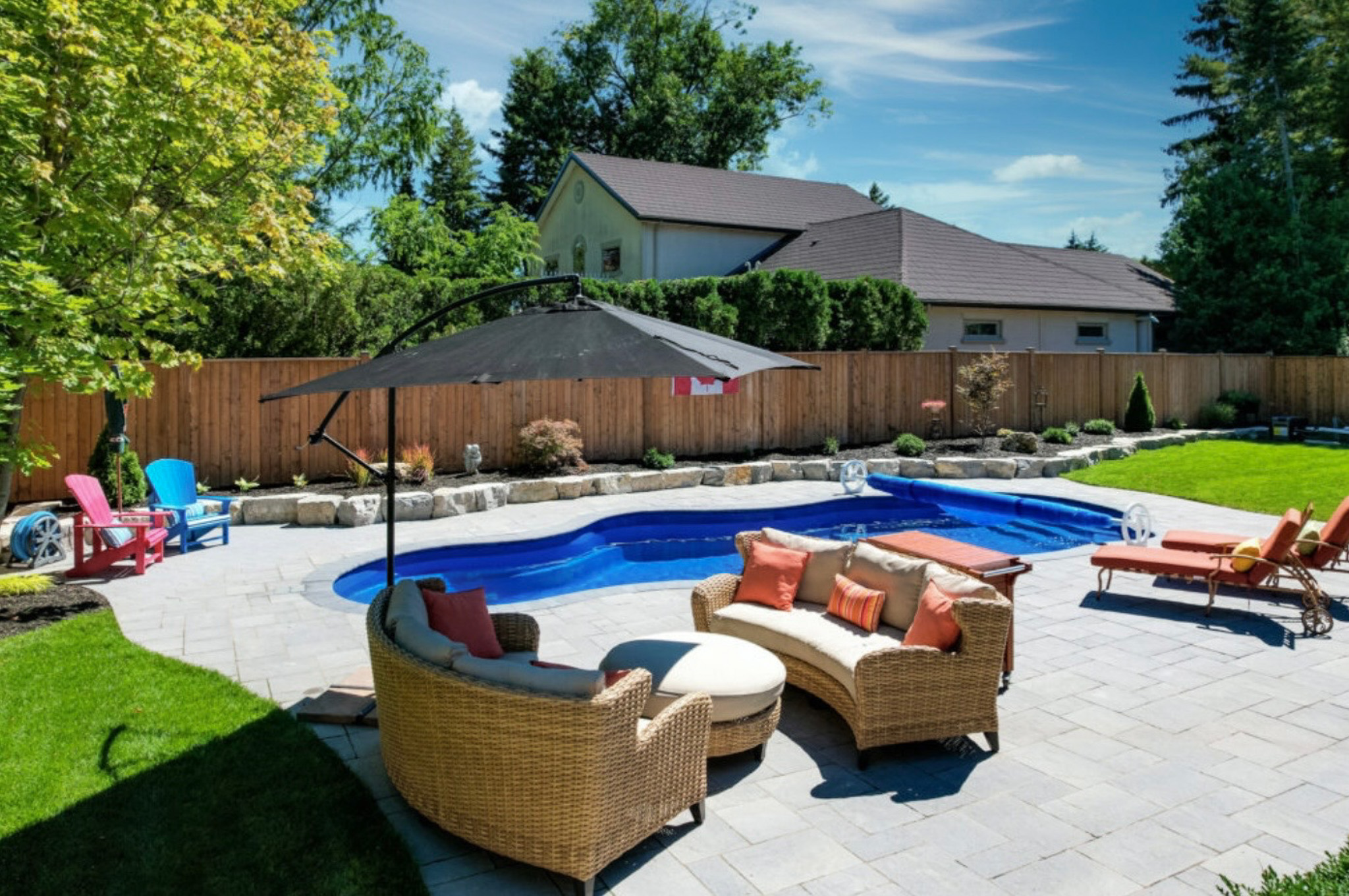 Backyard with a curved pool, wide paver patio, and wicker lounge seating